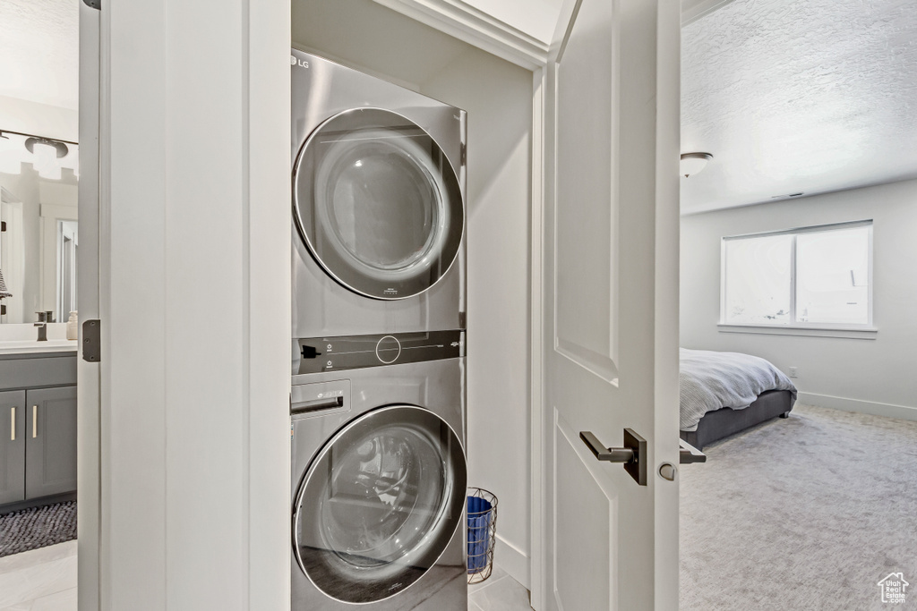 Laundry room featuring stacked washer / dryer, carpet flooring, and baseboards
