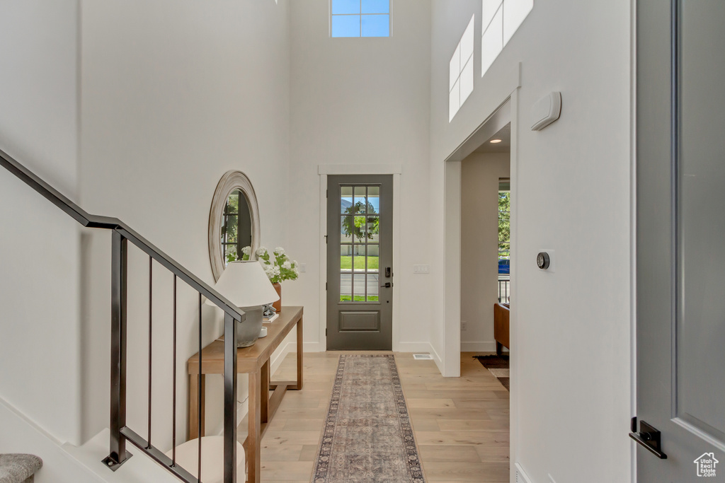 Entryway with plenty of natural light, light wood-style flooring, a high ceiling, stairs, and baseboards