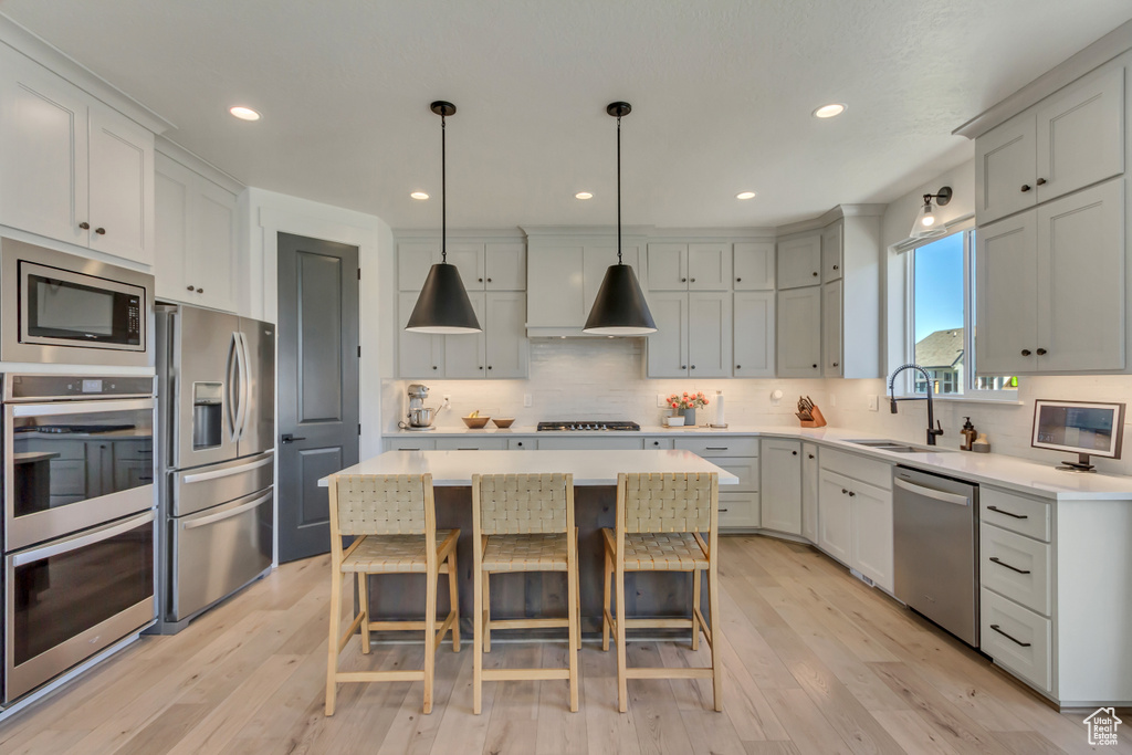 Kitchen featuring stainless steel appliances, a sink, a kitchen island, tasteful backsplash, and light wood-style flooring