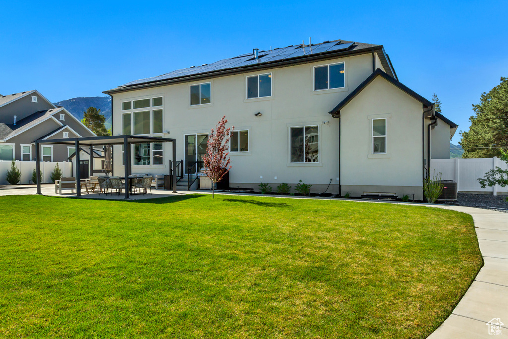 Rear view of house with roof mounted solar panels, a patio area, stucco siding, and a mountain view
