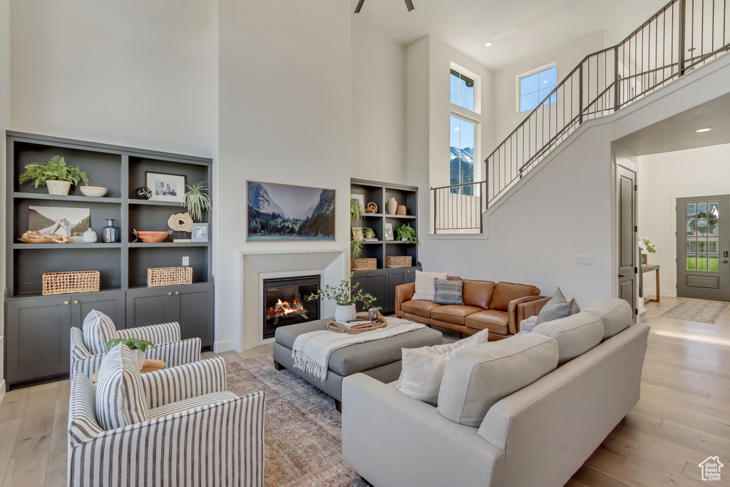 Living area featuring a high ceiling, plenty of natural light, light wood-type flooring, a glass covered fireplace, and recessed lighting