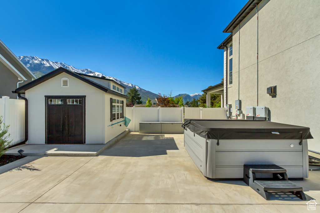 View of patio / terrace featuring a mountain view, a hot tub, a fenced backyard, and an outbuilding