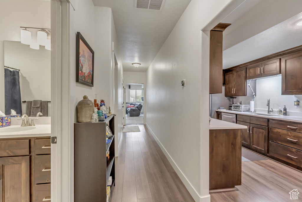 Kitchen with a sink, light wood-type flooring, light countertops, and stainless steel dishwasher