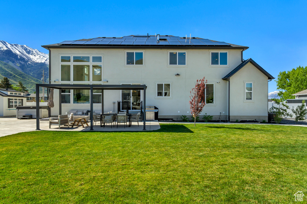 Rear view of property featuring stucco siding, solar panels, a yard, a mountain view, and a patio area