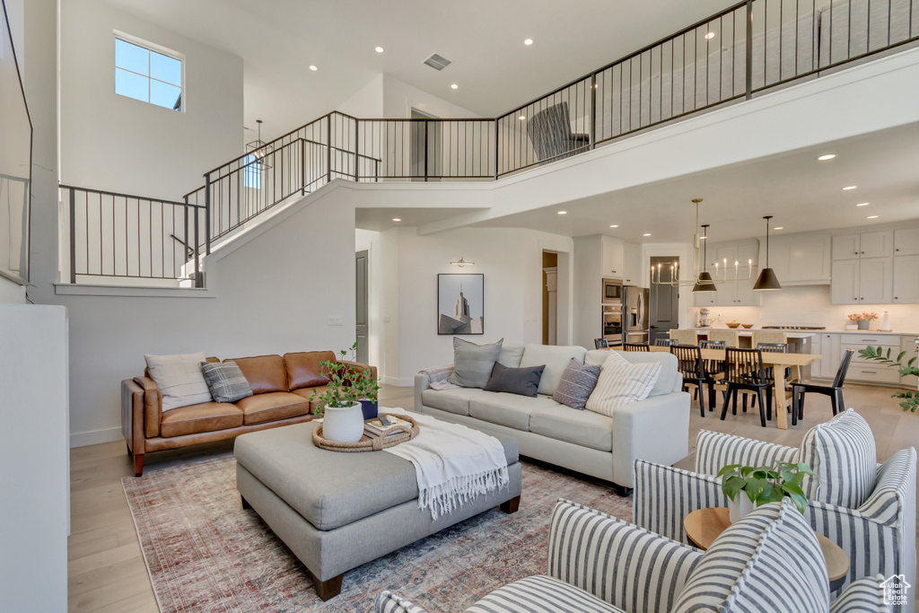 Living room with light wood-type flooring, a towering ceiling, stairway, recessed lighting, and baseboards