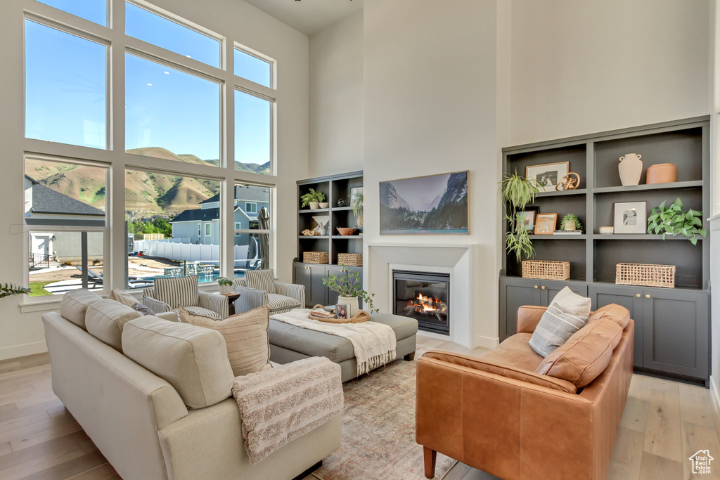 Living room with a towering ceiling, light wood-style floors, a glass covered fireplace, and baseboards