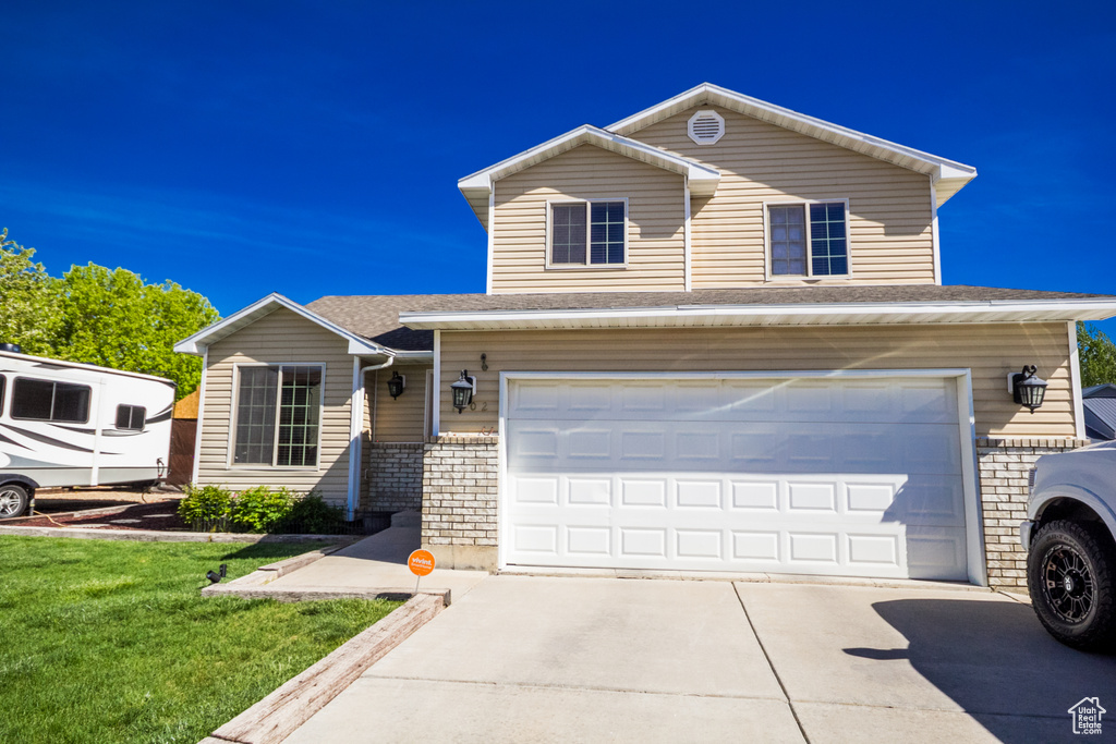 Traditional-style house featuring an attached garage, concrete driveway, a front yard, and roof with shingles