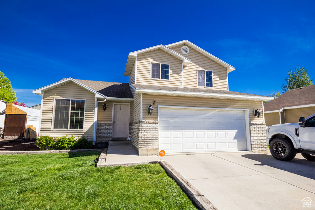 Traditional-style house with a garage, driveway, a front yard, and a shingled roof