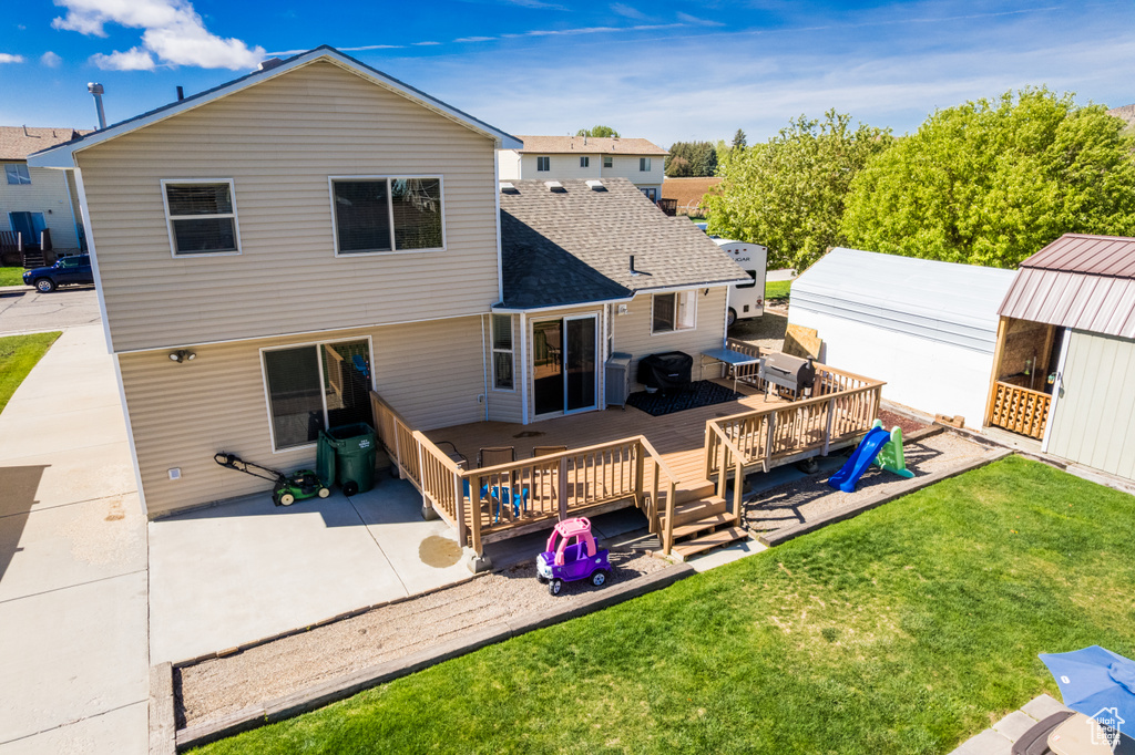 Rear view of house featuring a yard, a wooden deck, and a shingled roof