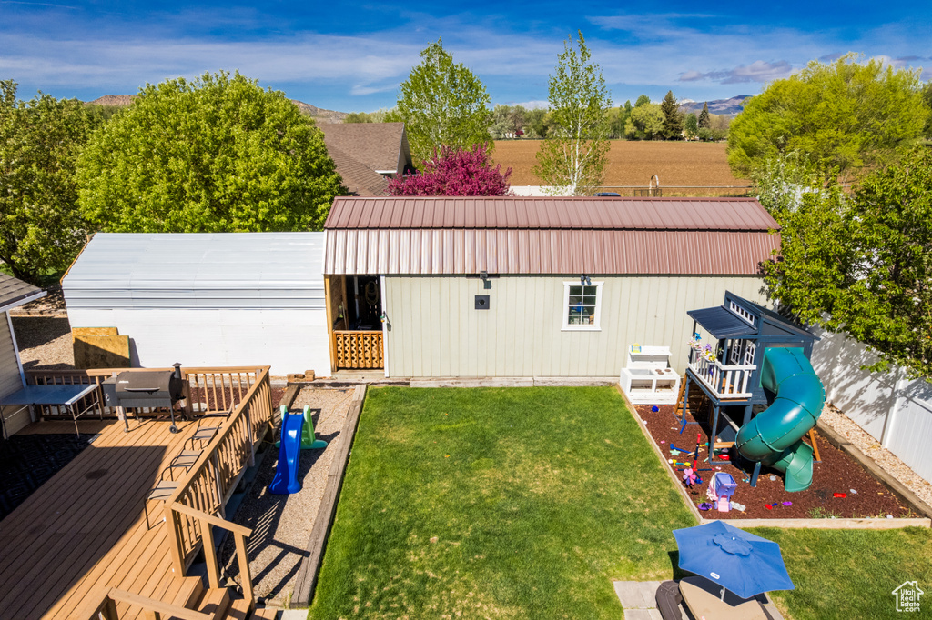 Back of house with a deck, a lawn, a playground, and metal roof