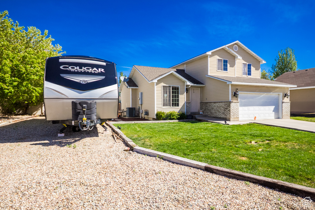 View of front of home featuring brick siding, concrete driveway, a garage, a front yard, and central AC unit