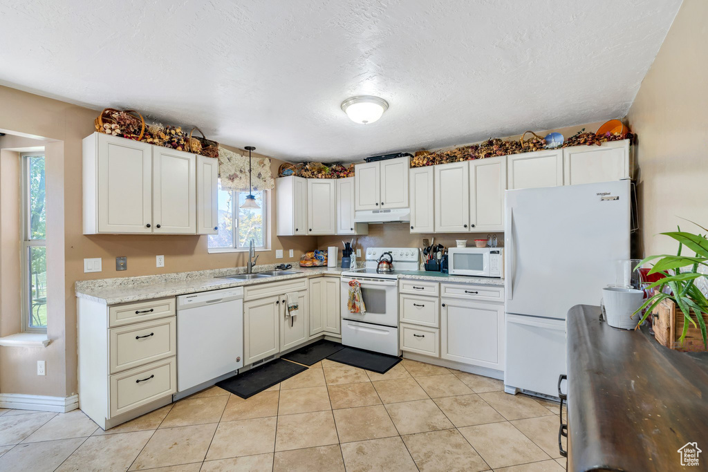 Kitchen featuring white appliances, under cabinet range hood, a sink, light tile patterned flooring, and pendant lighting