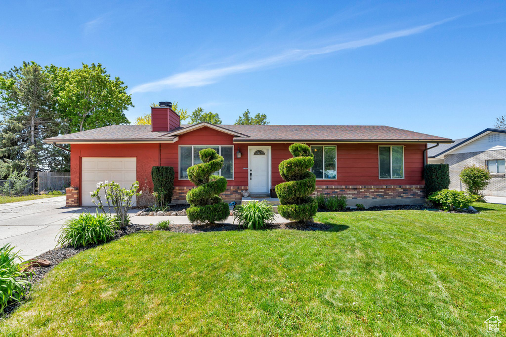 Ranch-style home with an attached garage, a chimney, driveway, a front lawn, and brick siding