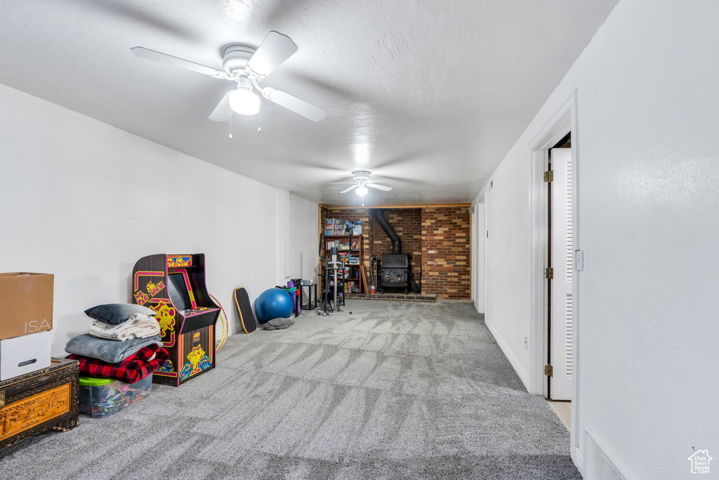 Recreation room featuring a wood stove, carpet, ceiling fan, and a textured ceiling