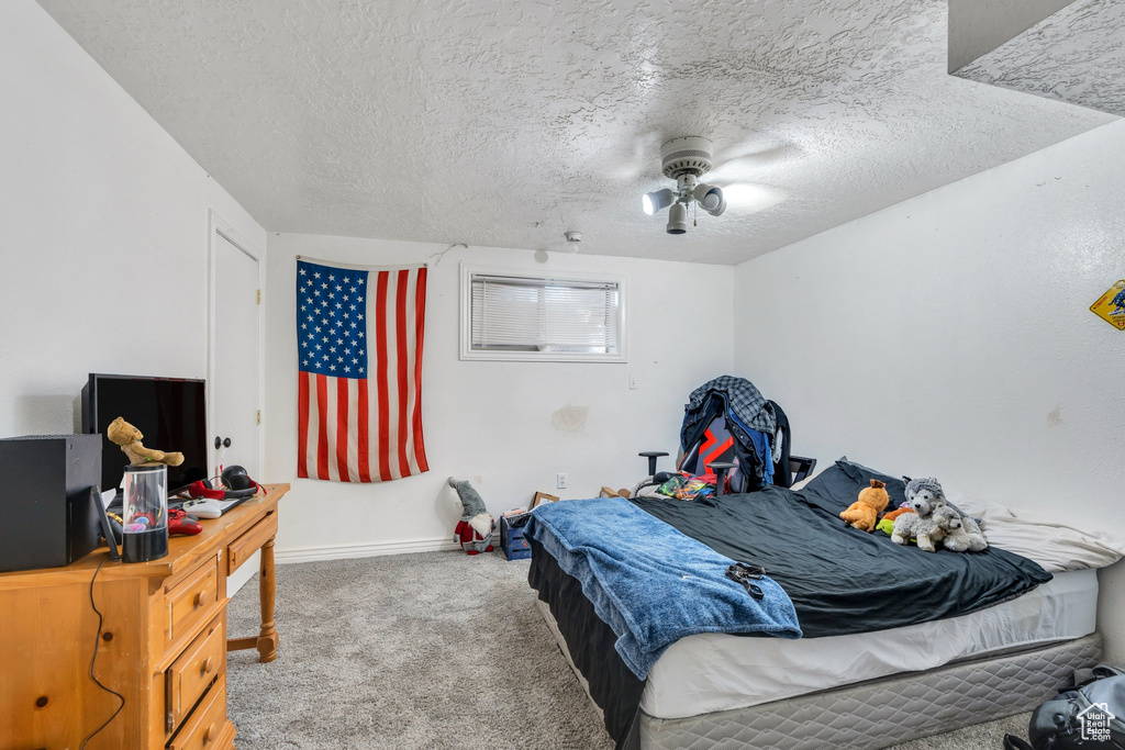 Carpeted bedroom with a textured ceiling, baseboards, and a ceiling fan