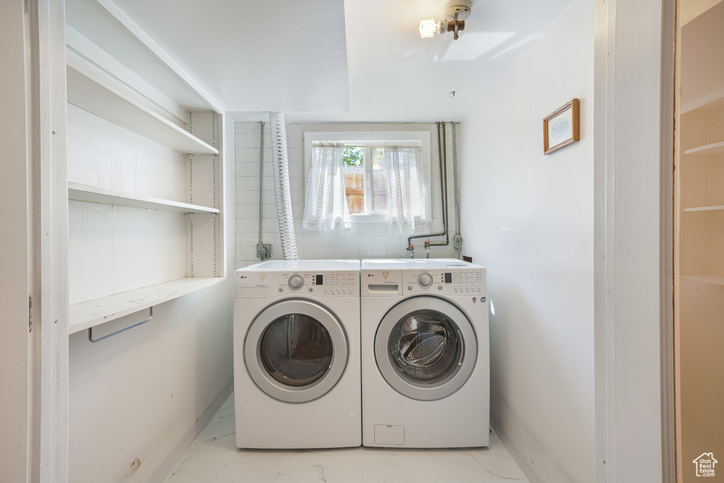 Washroom with washing machine and clothes dryer, light marble finish flooring, and baseboards