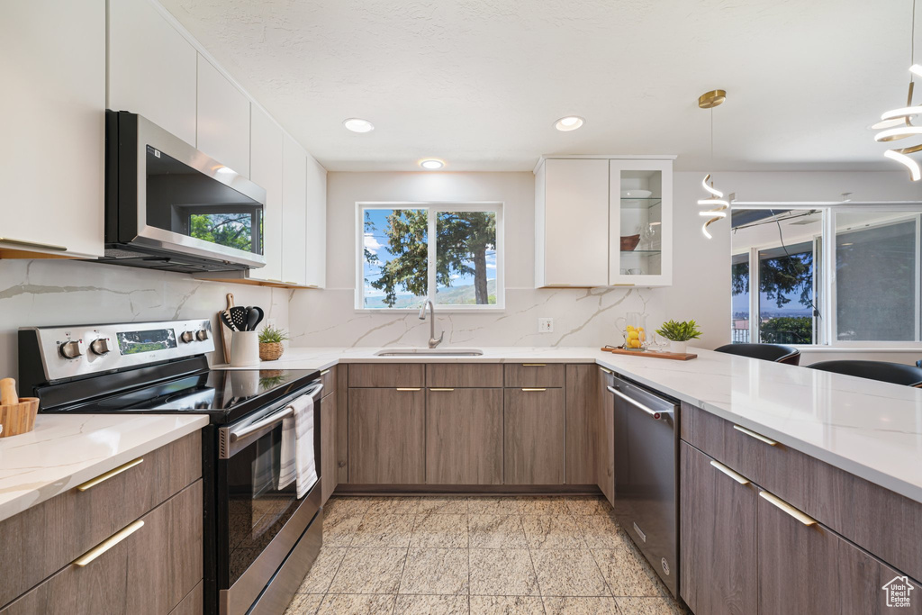 Kitchen featuring stainless steel appliances, a sink, granite floors, backsplash, and white cabinetry
