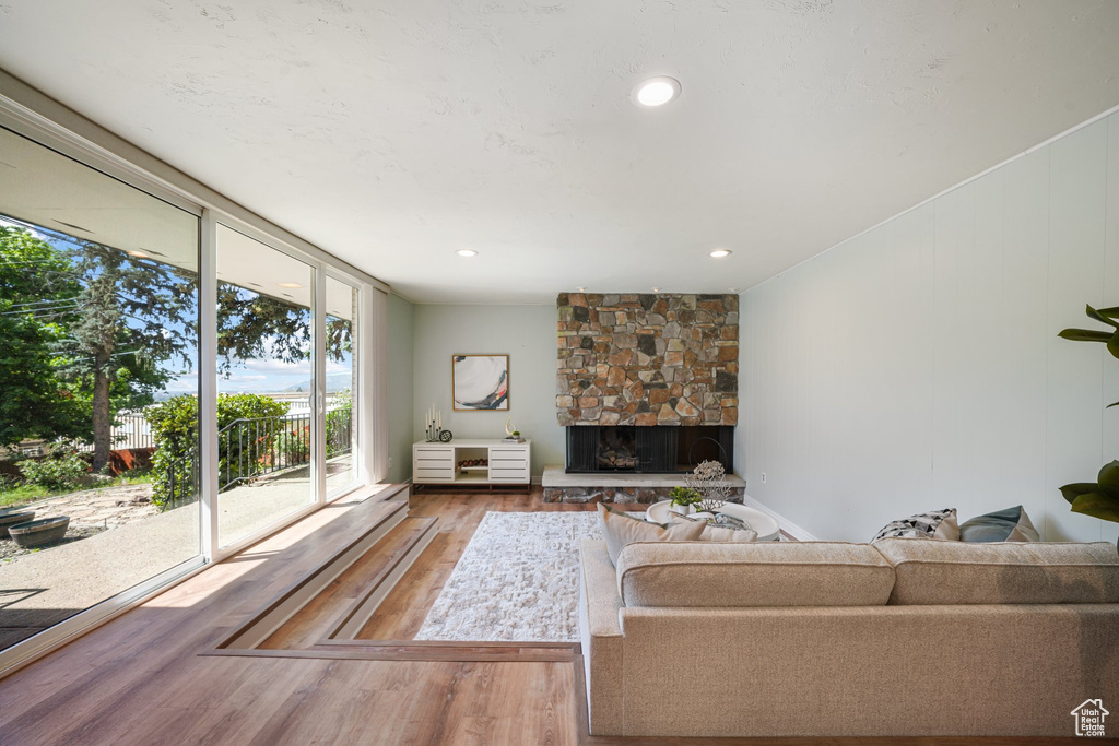 Living room with wood finished floors, a stone fireplace, recessed lighting, and expansive windows