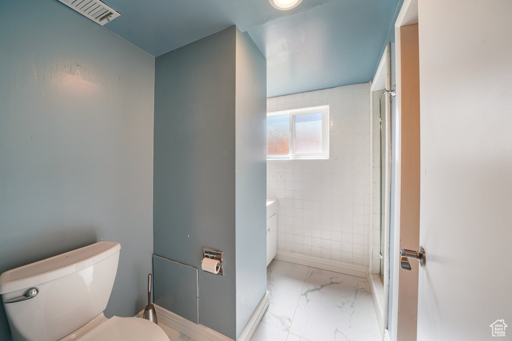 Full bath with marble look tiles, toilet, a shower, and baseboards