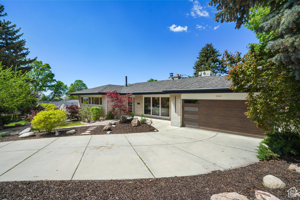 Ranch-style house with a garage, driveway, brick siding, and roof with shingles