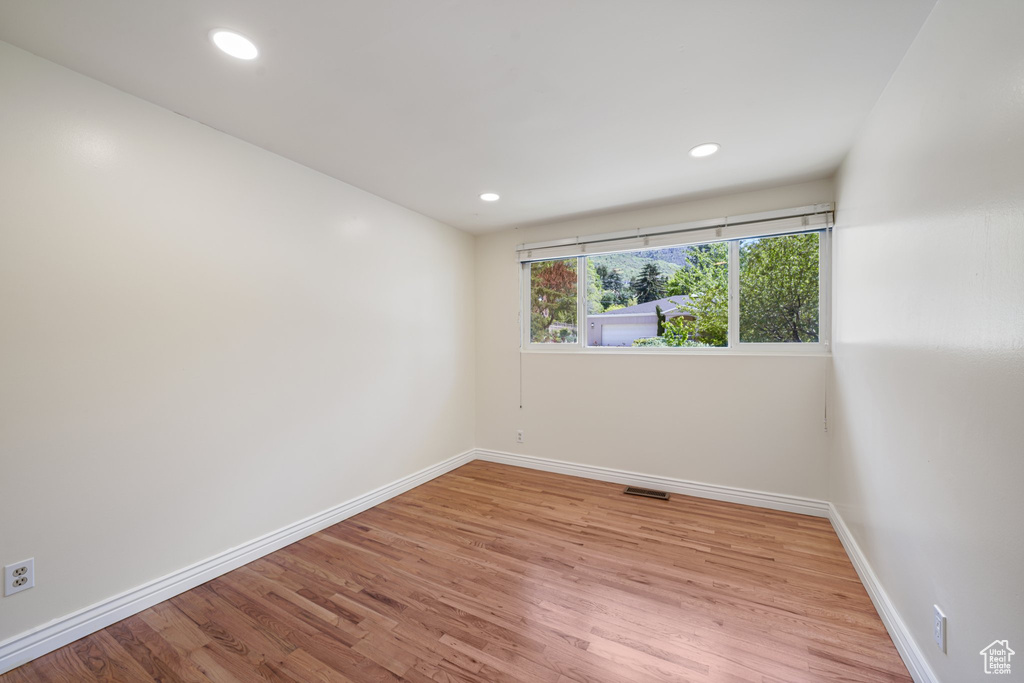 Empty room featuring baseboards, light wood-type flooring, and recessed lighting