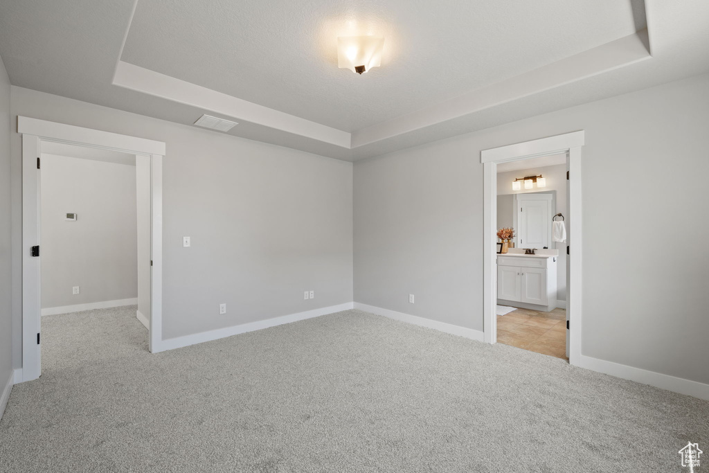 Empty room featuring a tray ceiling, light colored carpet, and baseboards