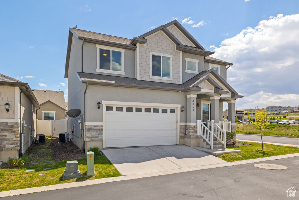 Craftsman-style house featuring a garage, stone siding, fence, concrete driveway, and cooling unit