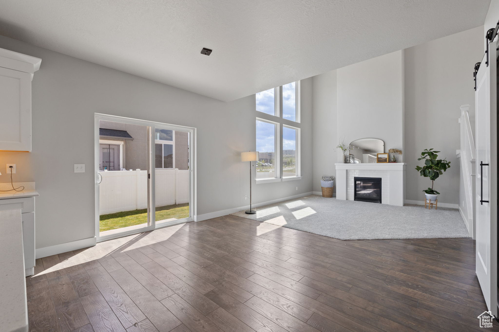 Unfurnished living room with a barn door, dark wood-style flooring, baseboards, and a glass covered fireplace