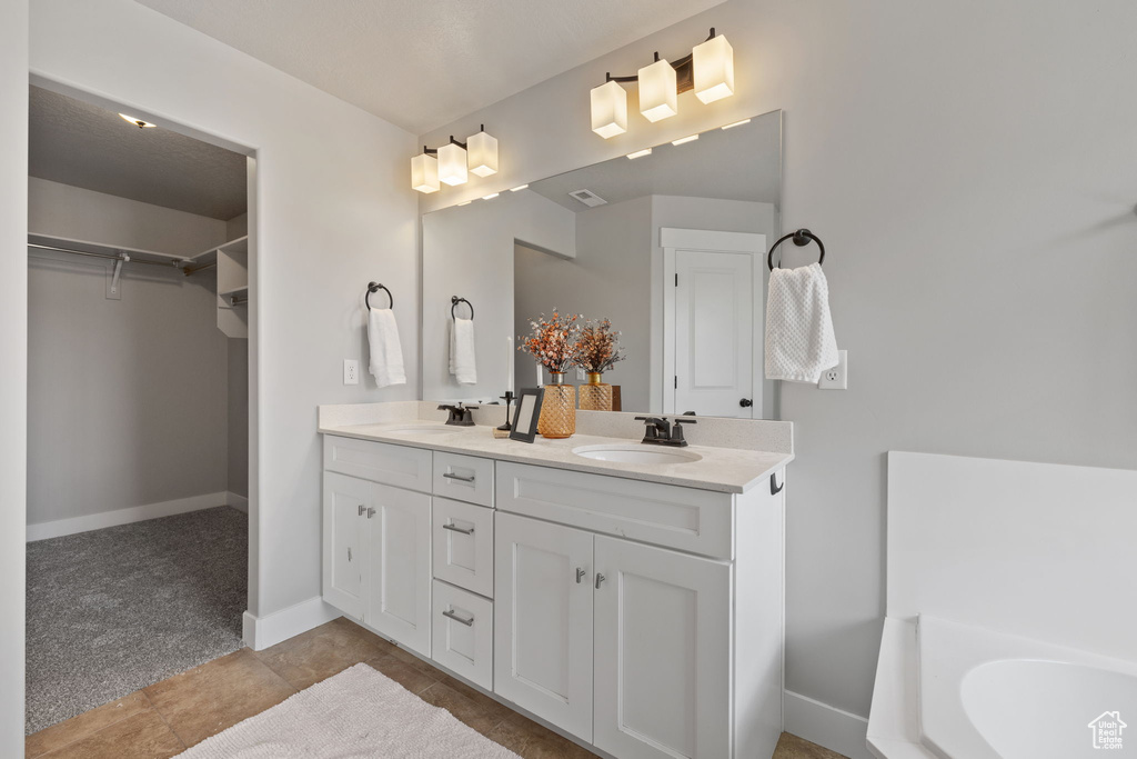Bathroom featuring a walk in closet, double vanity, baseboards, and a bathtub
