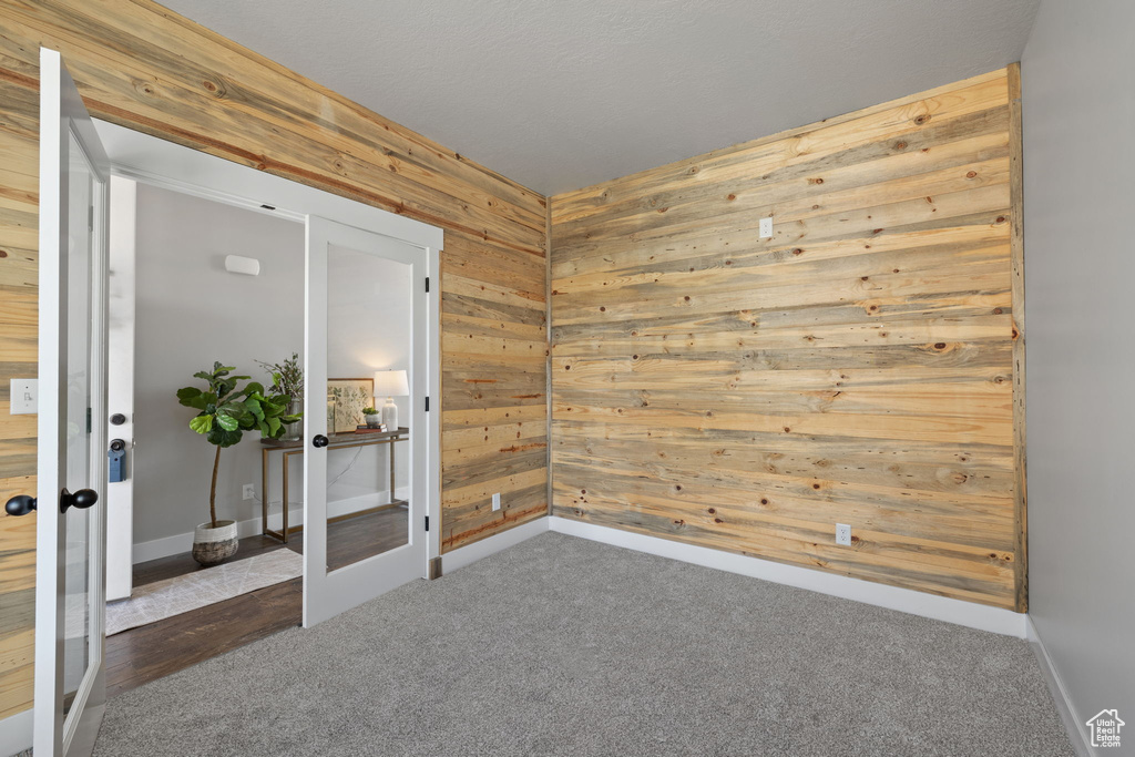 Spare room featuring wooden walls, carpet flooring, french doors, and baseboards