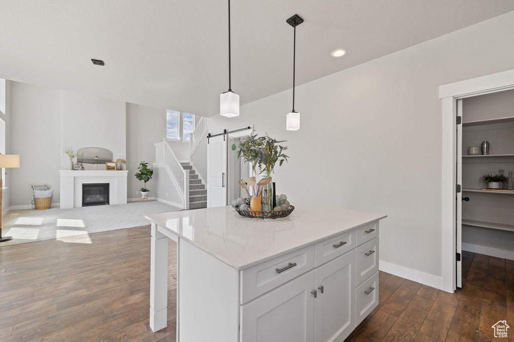 Kitchen featuring a barn door, dark wood-style flooring, decorative light fixtures, a center island, and baseboards