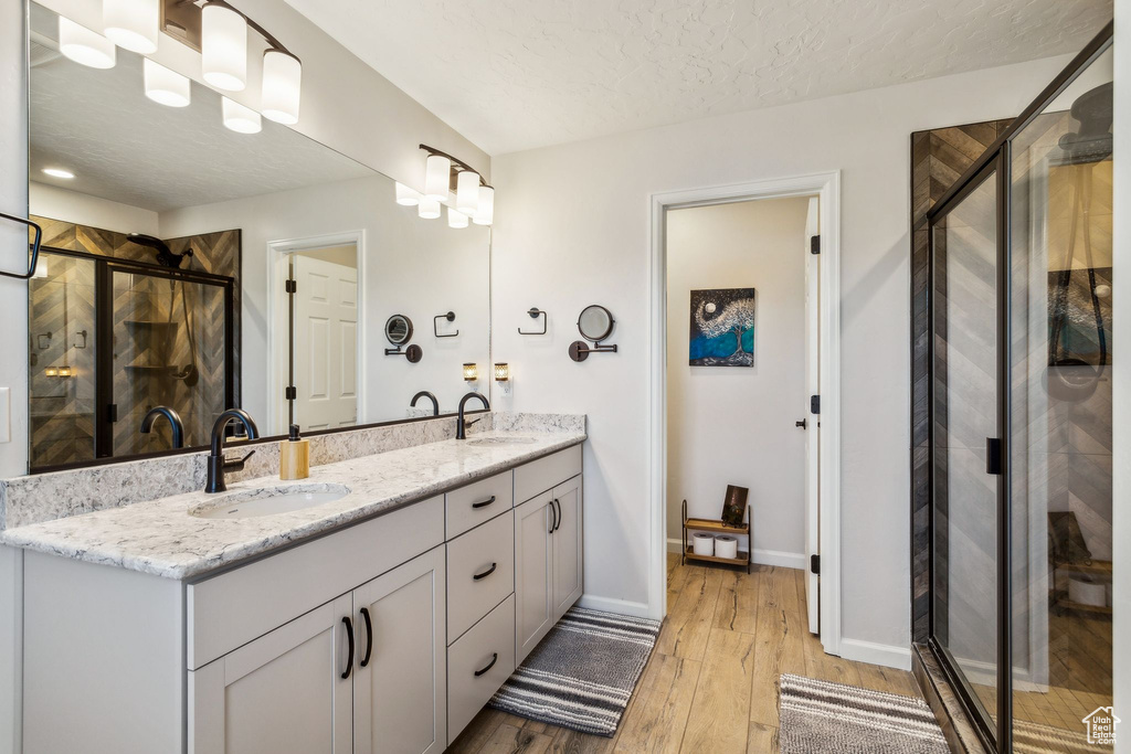 Bathroom featuring a stall shower, hardwood / wood-style flooring, double vanity, baseboards, and a textured ceiling