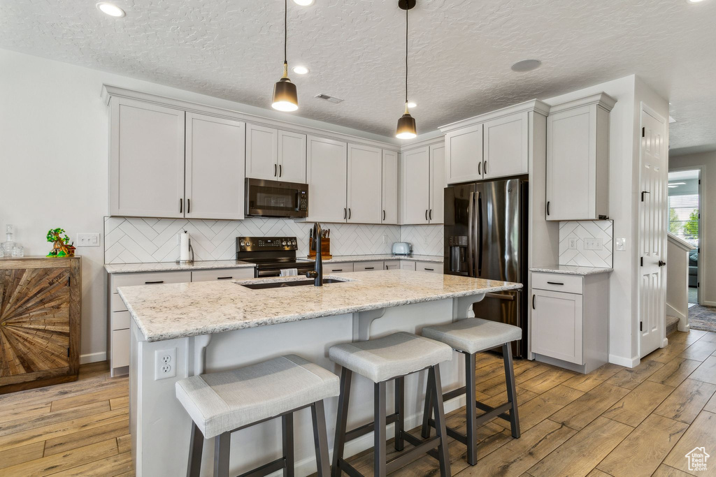 Kitchen with black electric range oven, refrigerator with ice dispenser, a sink, light wood finished floors, and a kitchen breakfast bar