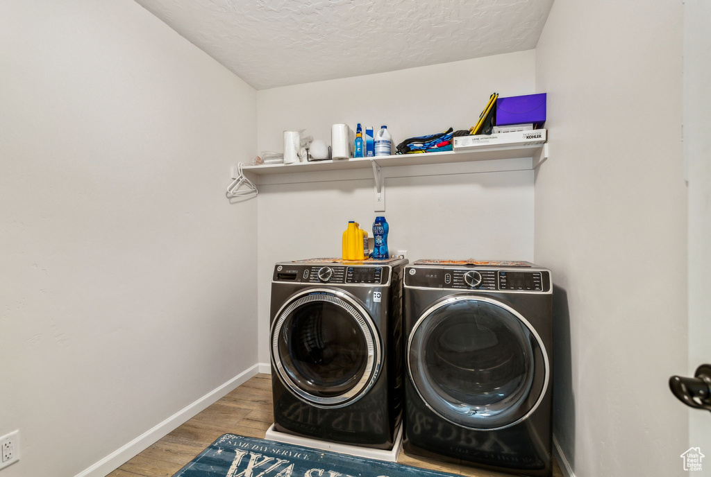 Washroom featuring independent washer and dryer, wood finished floors, a textured ceiling, and baseboards