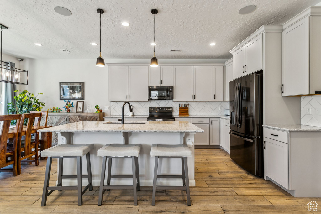 Kitchen with black appliances, a sink, light wood finished floors, decorative backsplash, and a kitchen breakfast bar