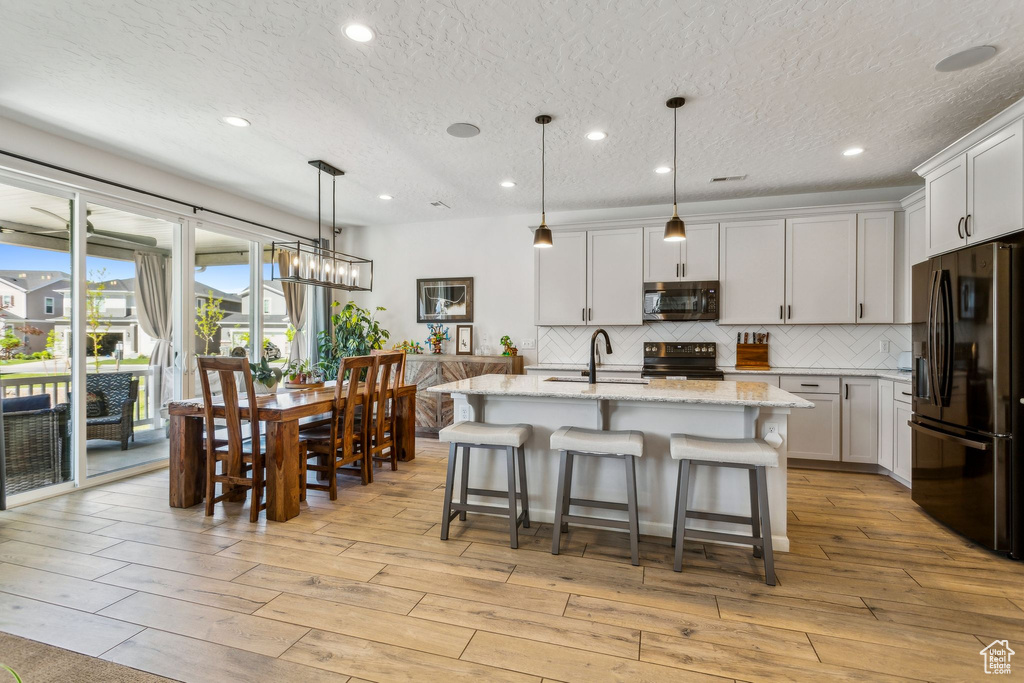 Kitchen featuring black appliances, a sink, tasteful backsplash, light stone countertops, and a textured ceiling