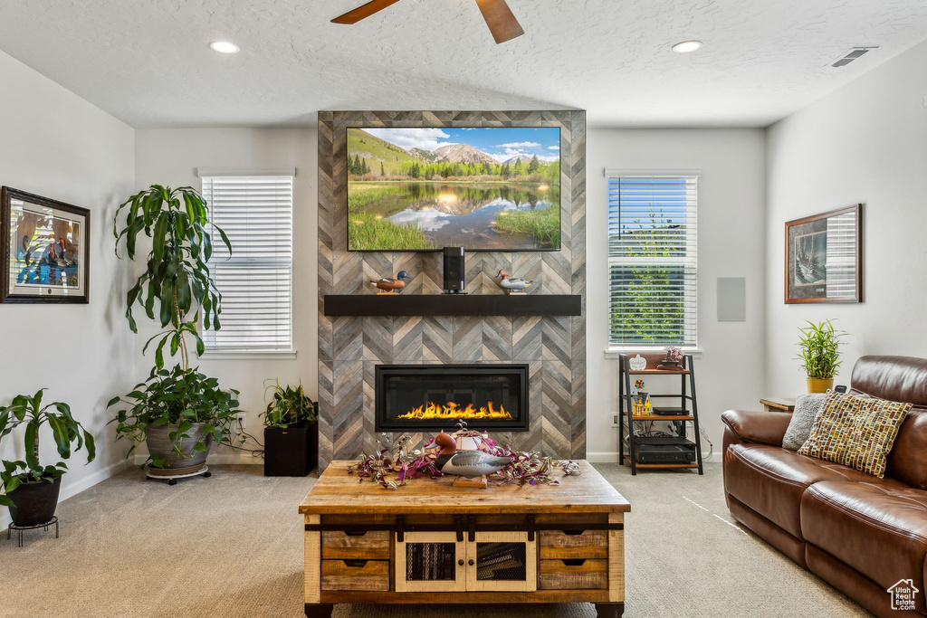 Living room featuring carpet flooring, baseboards, a ceiling fan, a textured ceiling, and a large fireplace