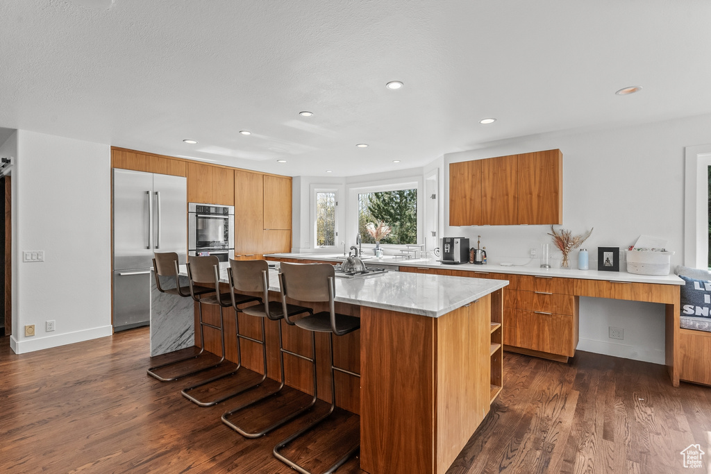 Kitchen featuring modern cabinets, appliances with stainless steel finishes, dark wood-style floors, recessed lighting, and a breakfast bar