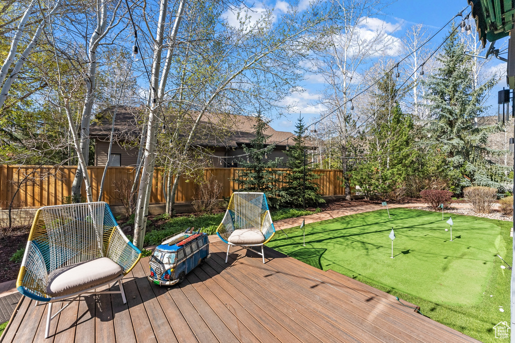 Wooden terrace with a putting area and a fenced backyard