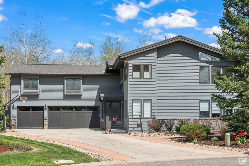 View of front of house with an attached garage, concrete driveway, and roof with shingles