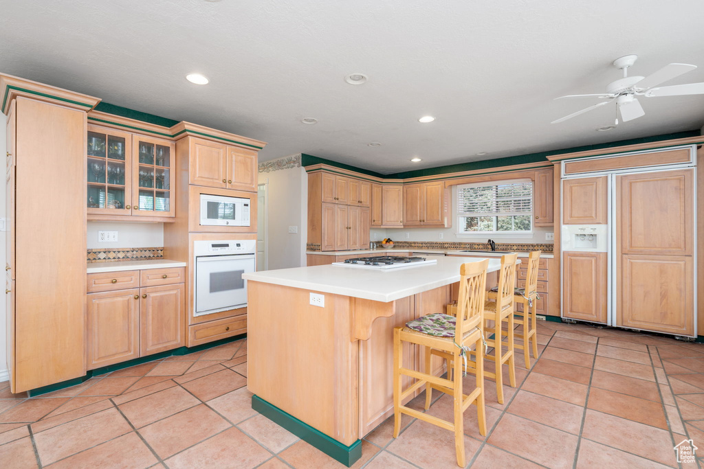 Kitchen with built in appliances, light brown cabinetry, a kitchen island, a breakfast bar area, and light countertops