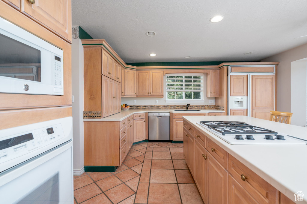 Kitchen with white appliances, light countertops, a sink, recessed lighting, and light brown cabinetry