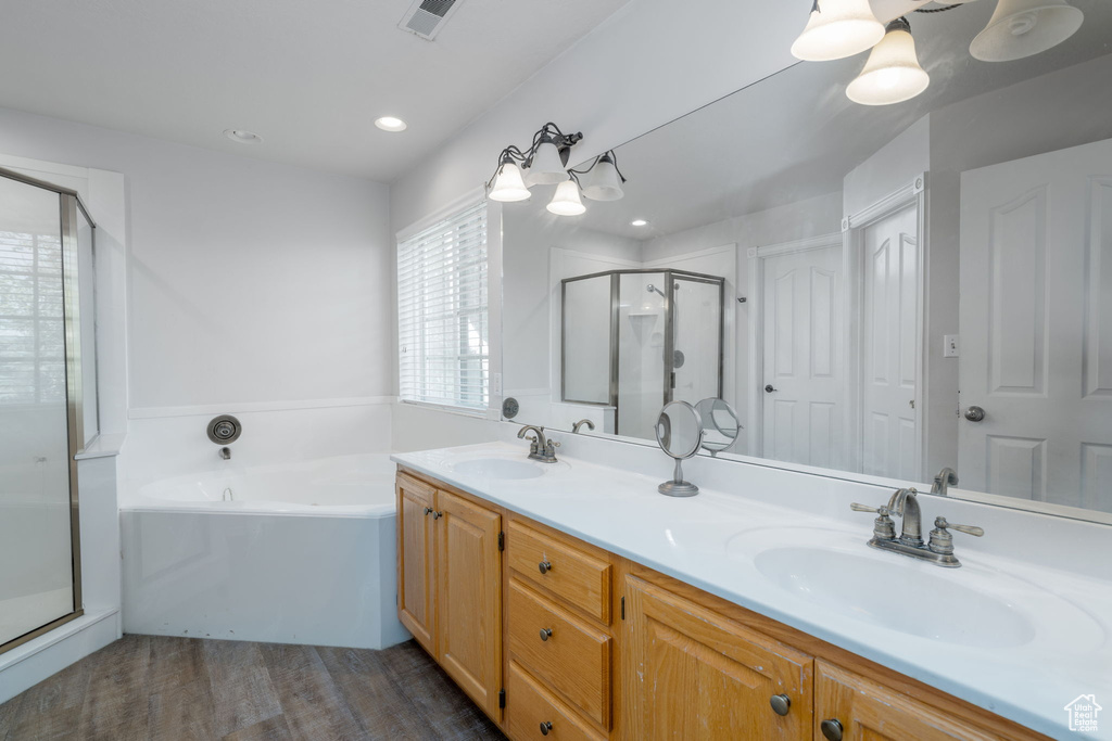 Bathroom featuring wood finished floors, a stall shower, double vanity, a bath, and recessed lighting