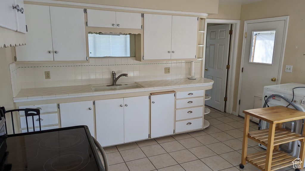 Kitchen with black electric range oven, a sink, tasteful backsplash, light tile patterned floors, and white cabinetry
