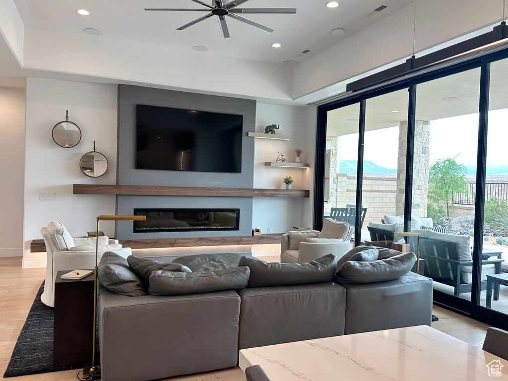 Living room featuring ceiling fan, healthy amount of natural light, a glass covered fireplace, light wood-style flooring, and recessed lighting
