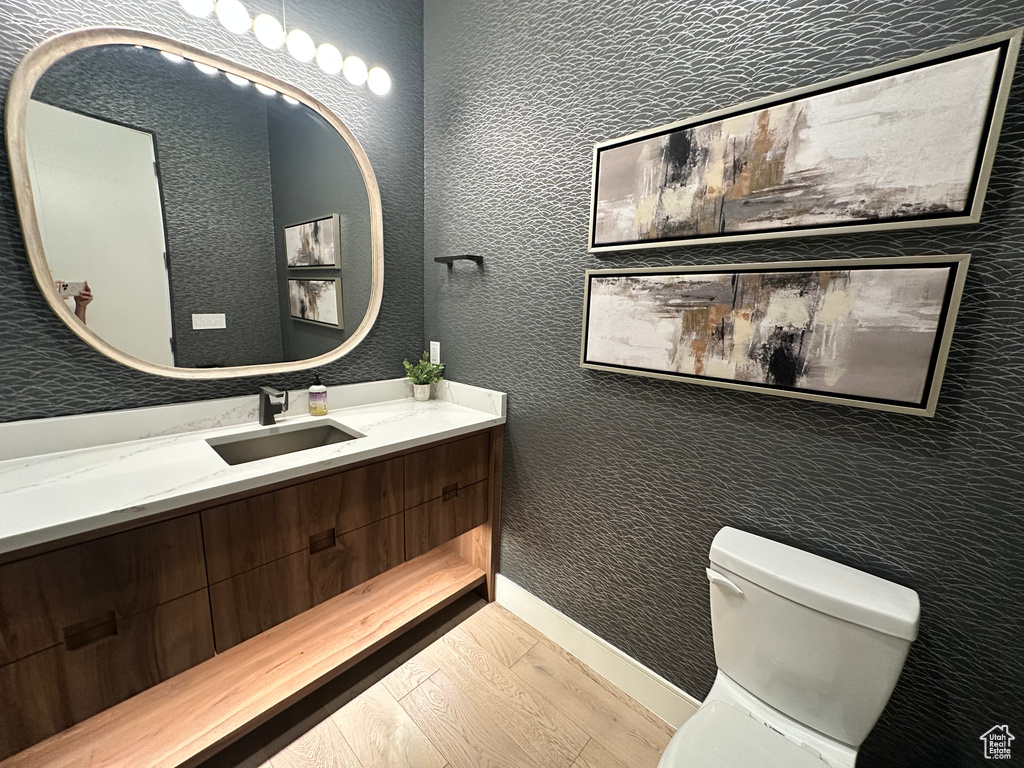 Half bath featuring wood finished floors, toilet, vanity, and baseboards