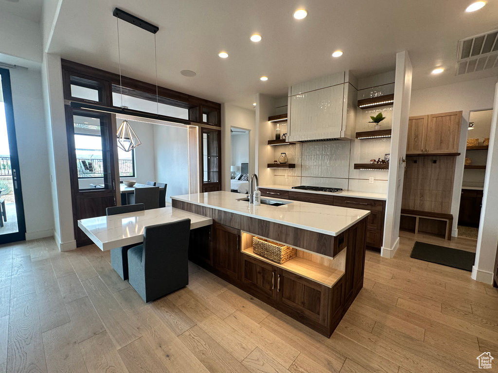 Kitchen featuring open shelves, a sink, light countertops, light wood-style floors, and a large island with sink