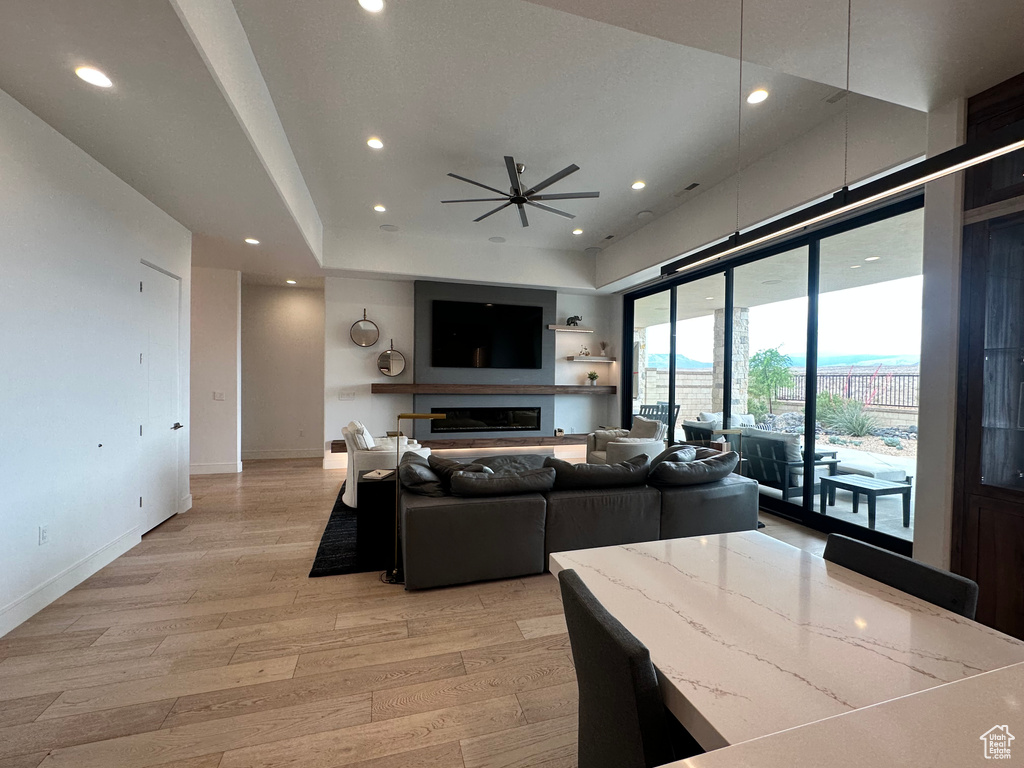 Living room featuring light wood-type flooring, recessed lighting, a ceiling fan, baseboards, and a glass covered fireplace