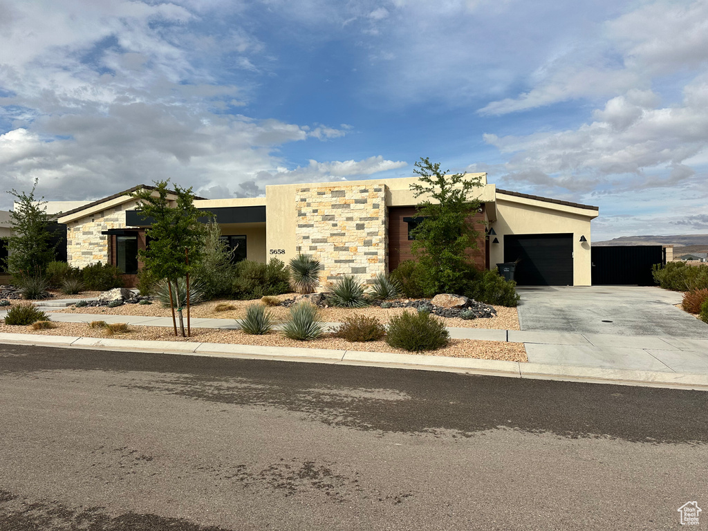 View of front of property with an attached garage, concrete driveway, stucco siding, and stone siding