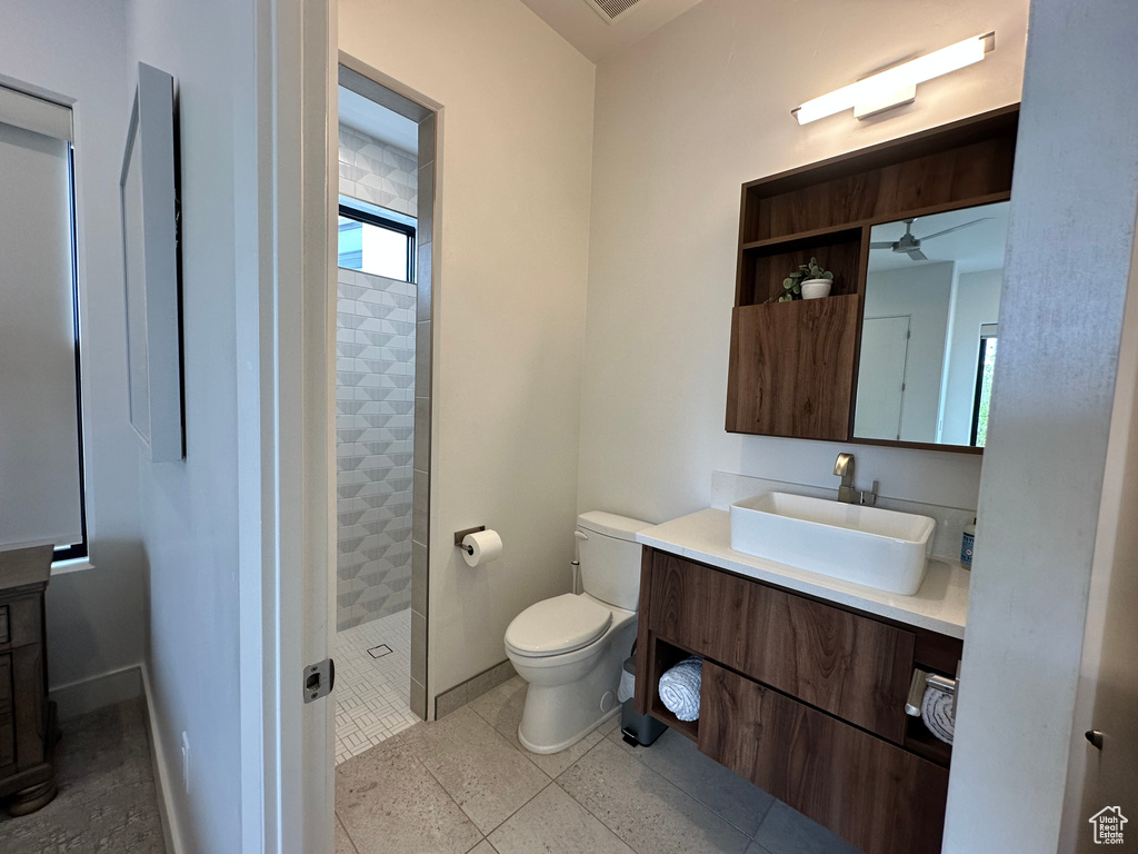 Full bathroom with tiled shower, vanity, toilet, ceiling fan, and baseboards